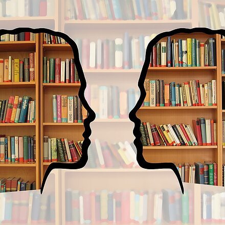 Silhouette zweier einander zugewandter Köpfe vor Bücherregal
